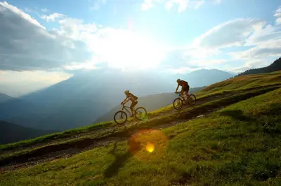 two people riding bikes on a grassy hill at Alpina Residence in Naturno
