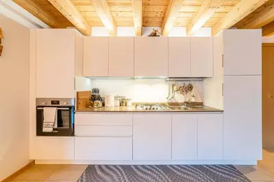 a white kitchen with white cabinets and a wooden ceiling at Charming Civetta in Alleghe