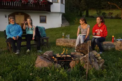 four women sitting around a fire in a yard at Gastreinhof in Meltina