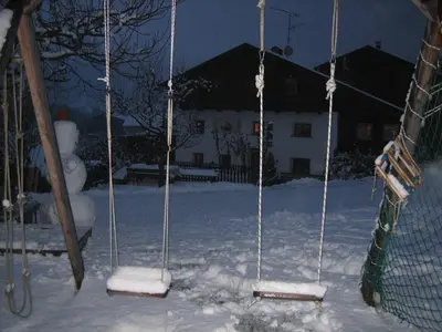 two swings in the snow with a house in the background at Lahnerhof in Campo Tures