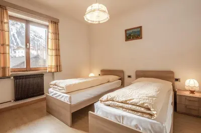 two beds in a bedroom with a window and a chandelier at Appartamento Blank in Arabba