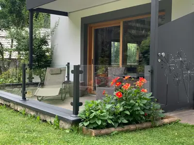 a house with a porch with a chair and flowers at Orchidea Suite & SPA Apartments in Canazei