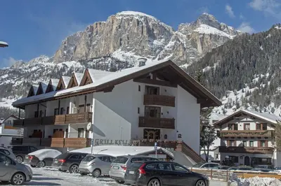 a building with cars parked in a parking lot in front of a mountain at GARNI AQUILA in Corvara in Badia