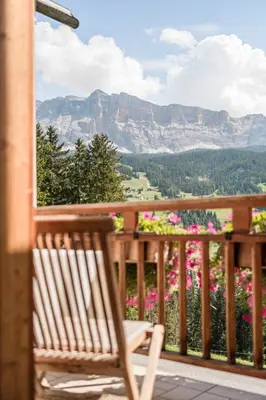 a wooden rocking chair sitting on a porch with flowers at Agriturismo Maso Runch in Badia
