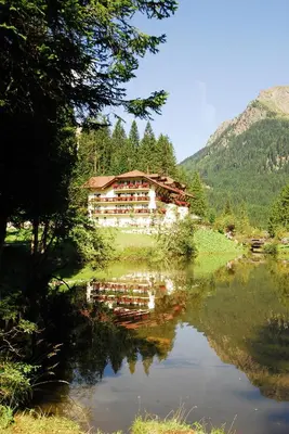 a house is reflected in a lake in the mountains at Hotel Plank in San Martino di Castrozza