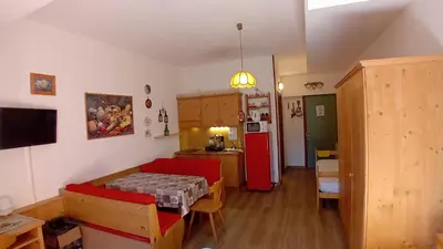 a kitchen and a living room with a table and a refrigerator at Tana delle Marmotte in Falcade