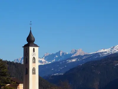 a clock tower with mountains in the background at B&B Signora Elvira in Capriana