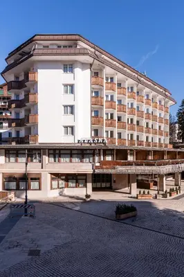 a woman standing on a balcony with snow covered mountains at Hotel Alaska Cortina in Cortina dʼAmpezzo