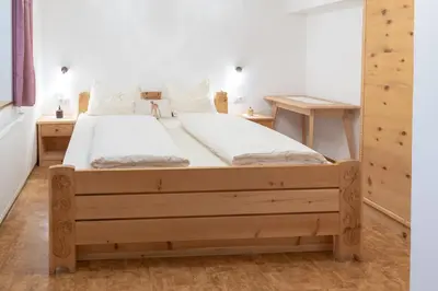 a bedroom with a wooden bed with white sheets at Apartments UDERA in Selva di Val Gardena