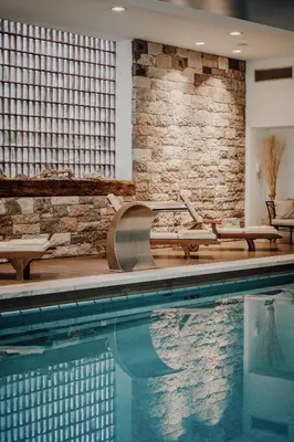a swimming pool with tables and chairs next to a brick wall at Hotel Adria in Merano