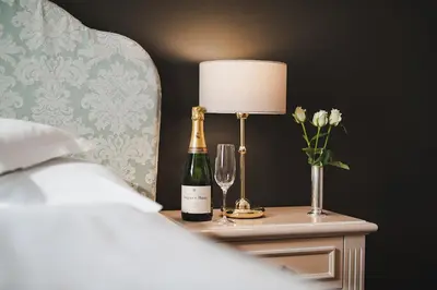 a bed with a bottle of champagne and a lamp on a table at Hotel Adria in Merano