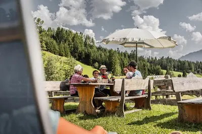 a group of people sitting at a picnic table under an umbrella at Lüch da Fusse in Badia