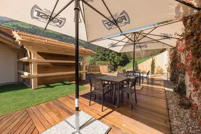 a patio with a table and chairs under an umbrella at Gitschberg - Appartements in Vandoies