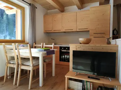 a dining room with a table and a tv and a kitchen at Tabiá sui Prá - appartamento monolocale Anna in Falcade