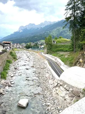a river next to a road with mountains in the background at EMARGHE, CASA A MOENA in Moena
