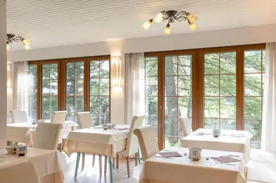 a restaurant with white tables and chairs and windows at B&B Garni Villa Campitello in Campitello di Fassa