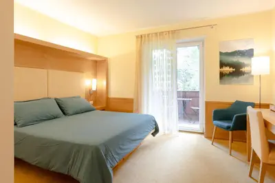 a bedroom with a bed and a window and a desk at B&B Garni Villa Campitello in Campitello di Fassa