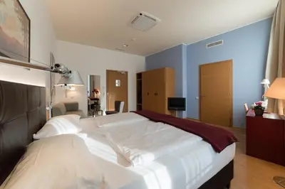 a bedroom with two white beds and a blue wall at Hotel Stiegl Scala in Bolzano