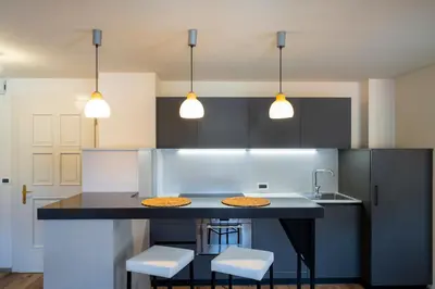 a kitchen with a black island with stools and lights at Ciasa Buro - Ron in Moena