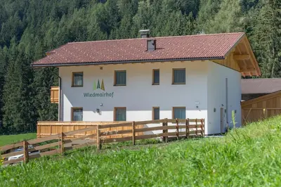 a white barn with a wooden fence in front of it at Wiedmairhof in Villa Ottone