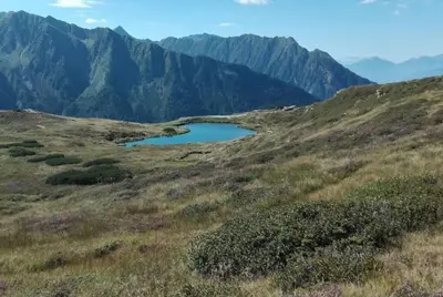a small lake on a hill with mountains in the background at Almgasthaus Flecknerhütte in San Leonardo in Passiria