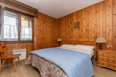 a bedroom with a bed and a wooden wall at Dimora al Vajolet in Pozza di Fassa