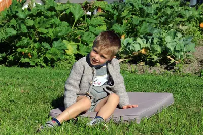 a young boy sitting on a mattress in the grass at Stiflerhof in Falzes