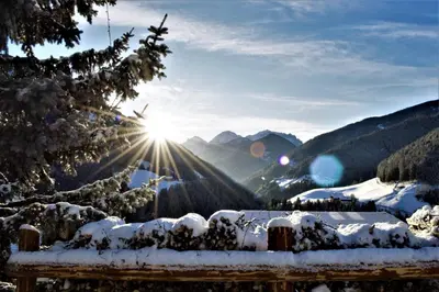 a bench covered in snow with the sun in the background at Hotel Onach in San Lorenzo di Sebato