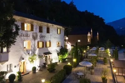a hotel with tables and umbrellas in a courtyard at night at Ansitz Gamp in Chiusa