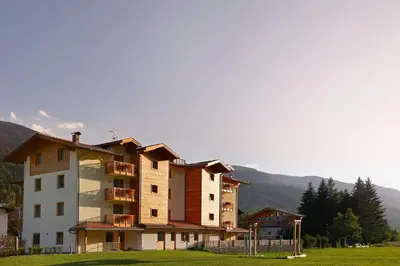 a building in a field with mountains in the background at Residence Nele in Ziano di Fiemme