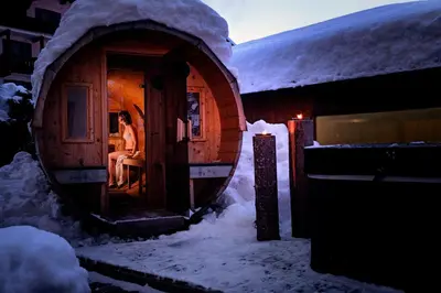 a woman sitting in the doorway of a small house in the snow at Residence Nele in Ziano di Fiemme
