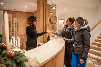 a group of three women shaking hands at a counter at Hotel Nele in Ziano di Fiemme
