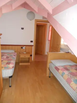 a bedroom with two beds and a staircase at Villetta Giumella in Pozza di Fassa