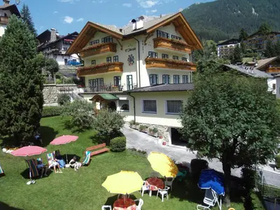 a large building with chairs and umbrellas in a yard at Hotel L'Ideale in Moena