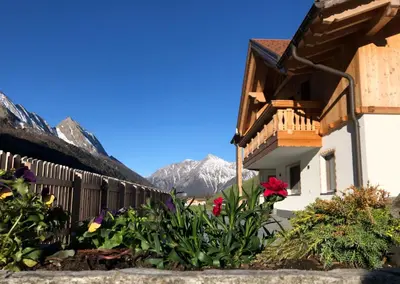 a building with flowers and mountains in the background at Ferienwohnungen Unterangerhof in Quinzo