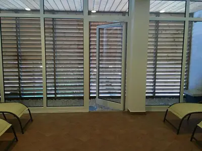 a room with windows with blinds and tables and chairs at Appartamento Alpe di Siusi in Alpe di Siusi