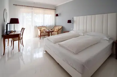 a white bedroom with a large bed and a table and chairs at Hotel Aster in Merano