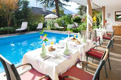 a restaurant with tables and chairs next to a swimming pool at Hotel Aster in Merano