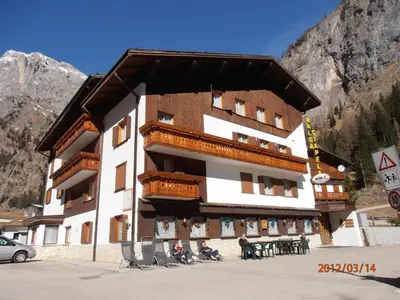 a building in the mountains with people sitting outside of it at Albergo Malga Ciapela in Rocca Pietore
