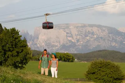 a man and a woman standing in a field with a ski lift at Hotel Regina in Soprabolzano