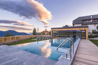a swimming pool with a wooden deck next to a building at Hotel Regina in Soprabolzano
