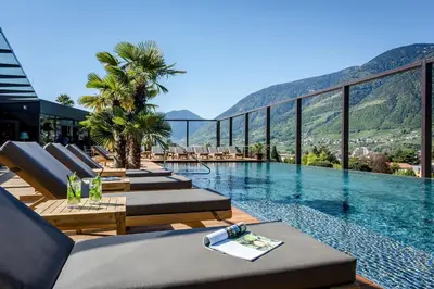 a pool with lounge chairs and a view of mountains at Hotel Therme Meran - Terme Merano in Merano