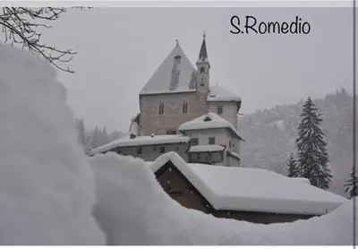 a snow covered building with a church in the background at Appartamento Da Romina con parcheggio gratuito in Sanzeno