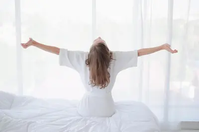 a young girl sitting on a bed with her arms outstretched at Bio & Wellnesshotel Pazeider - Healing Garden above Meran in Marlengo