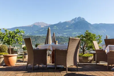 a patio with a table and chairs with mountains in the background at Bio & Wellnesshotel Pazeider - Healing Garden above Meran in Marlengo