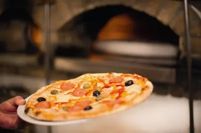 a person holding a small pizza on a plate at Aktiv & Genusshotel Lodenwirt in Vandoies