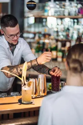 a man with a tattooacist making drinks at a bar at Aktiv & Genusshotel Lodenwirt in Vandoies