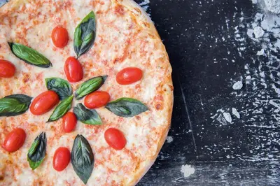 a pizza with tomatoes and basil on a table at Aktiv & Genusshotel Lodenwirt in Vandoies