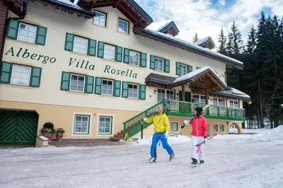 two people playing in the snow in front of a hotel at Hotel Villa Rosella Park & Wellness in Canazei