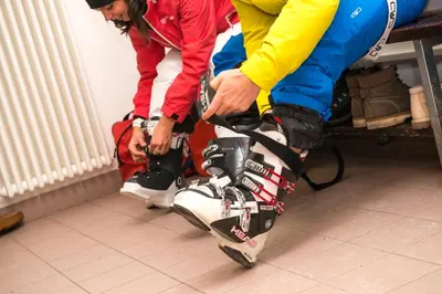 two people are putting on a pair of skis at Hotel Villa Rosella Park & Wellness in Canazei
